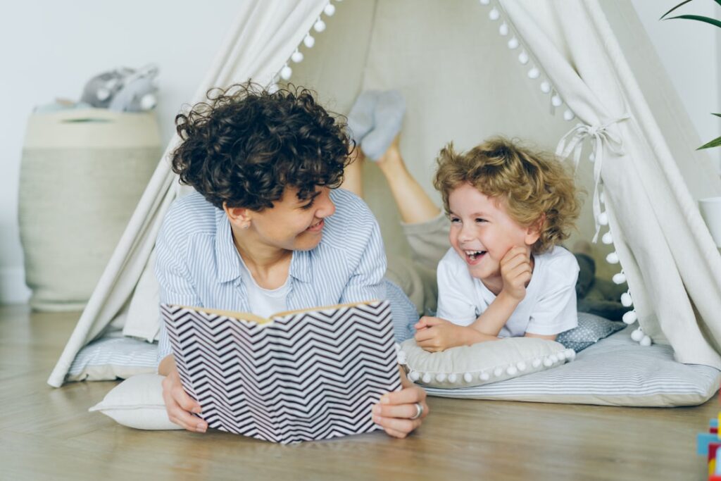 Parent and child read a book together at a kitchen table with letter cards and a notebook nearby.