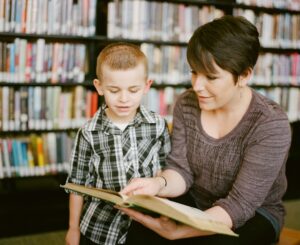 Child pointing to letters in a book while an adult listens at a kitchen table