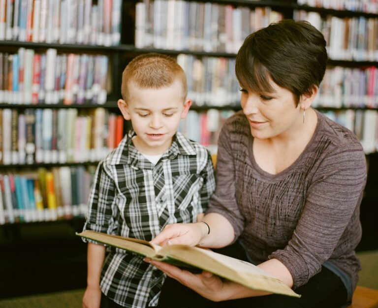Child pointing to letters in a book while an adult listens at a kitchen table