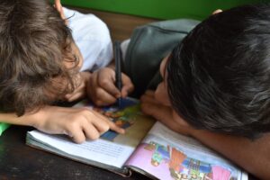 Student reading with an adult while a notebook and letter cards rest on the table.